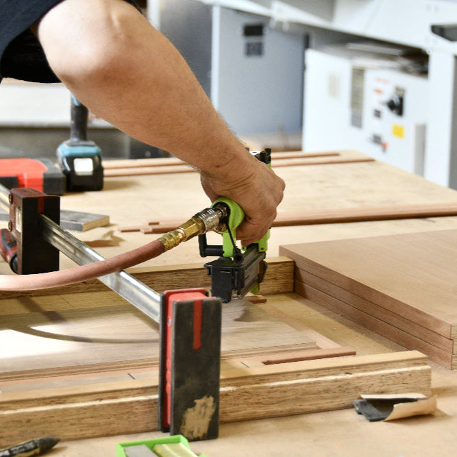 Person using a nail gun on wooden planks in a workshop setting