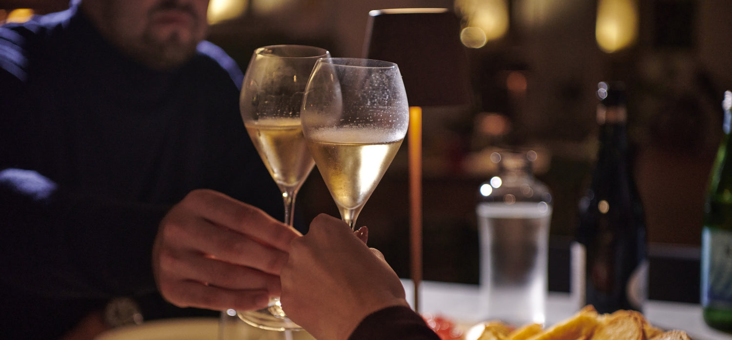 Two glasses of champagne being clinked together at a table with blurred background