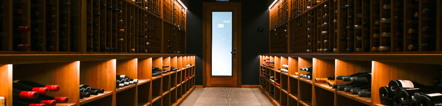 Wine cellar with rows of wine bottles illuminated by overhead lights.