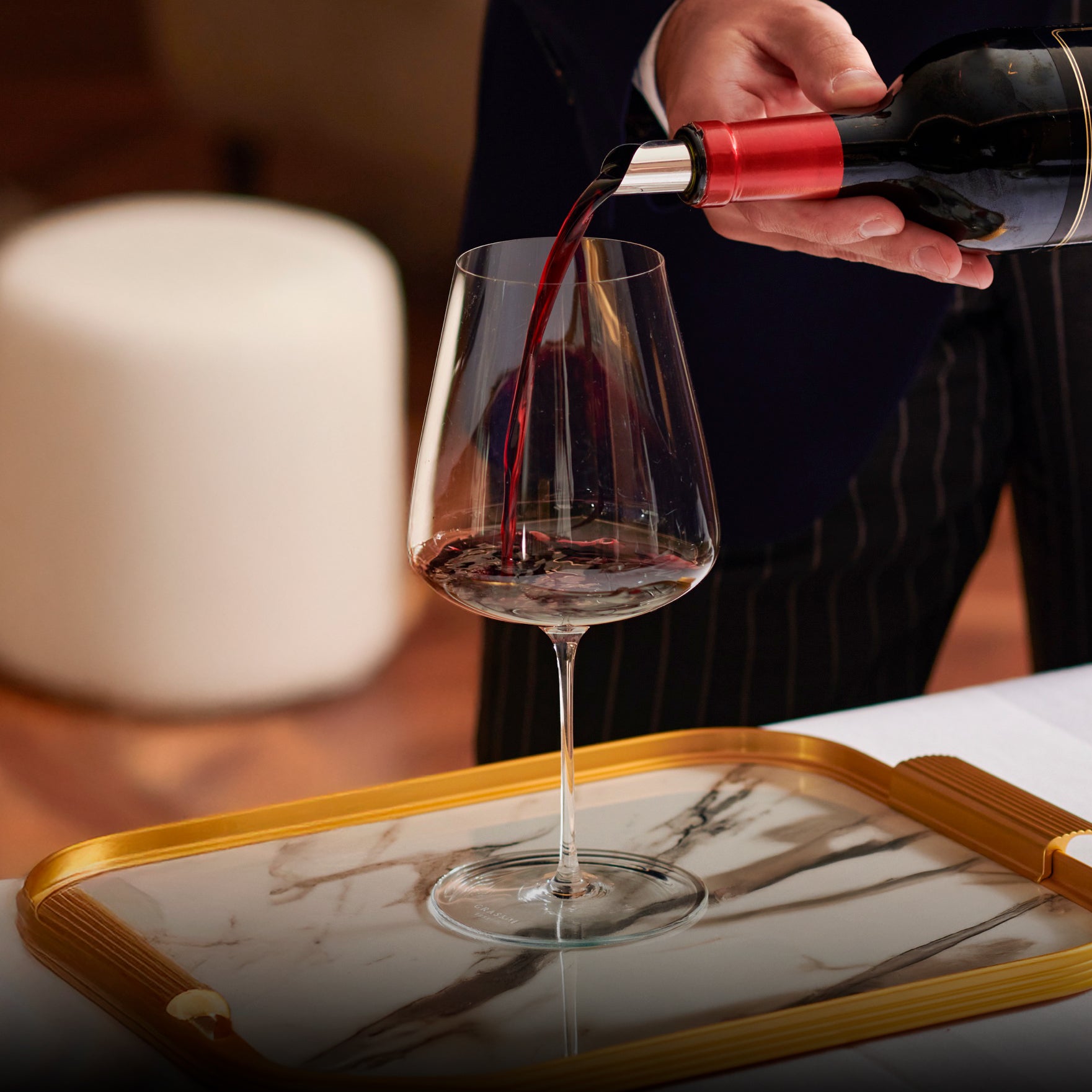 Person pouring red wine into a glass on a marble tray.