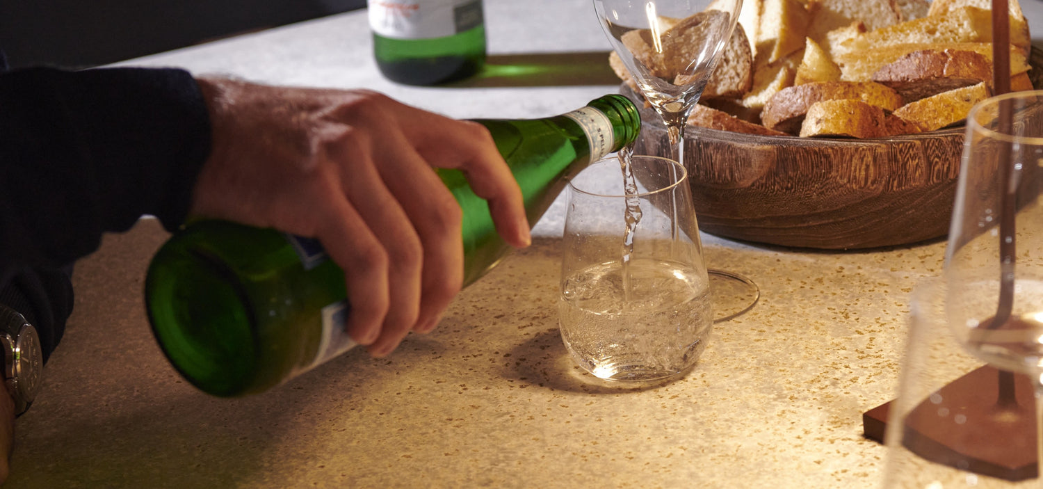 Person pouring green beer into a glass on a bar counter with bread and other items.