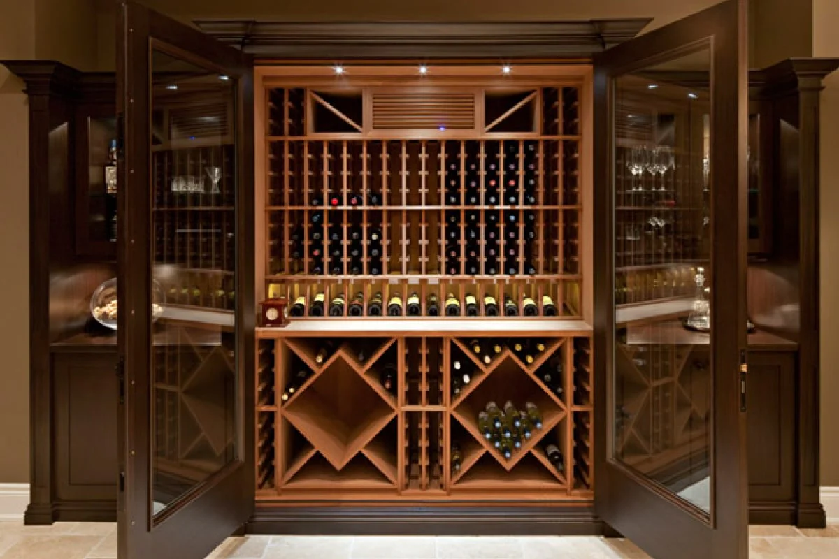 Wooden wine cellar with glass doors open, displaying rows of wine bottles.