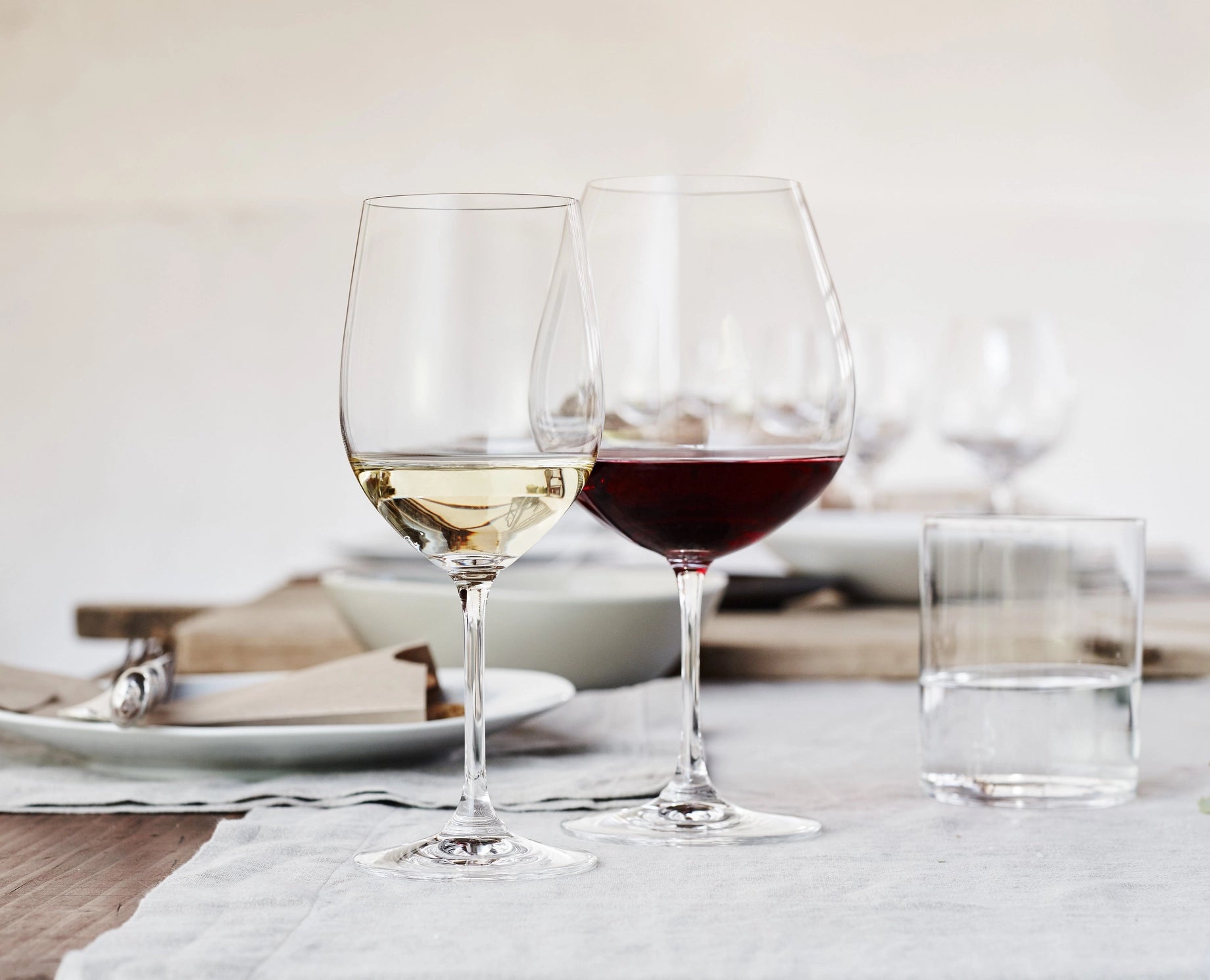 Two wine glasses, one with white wine and one with red wine, on a table setting.